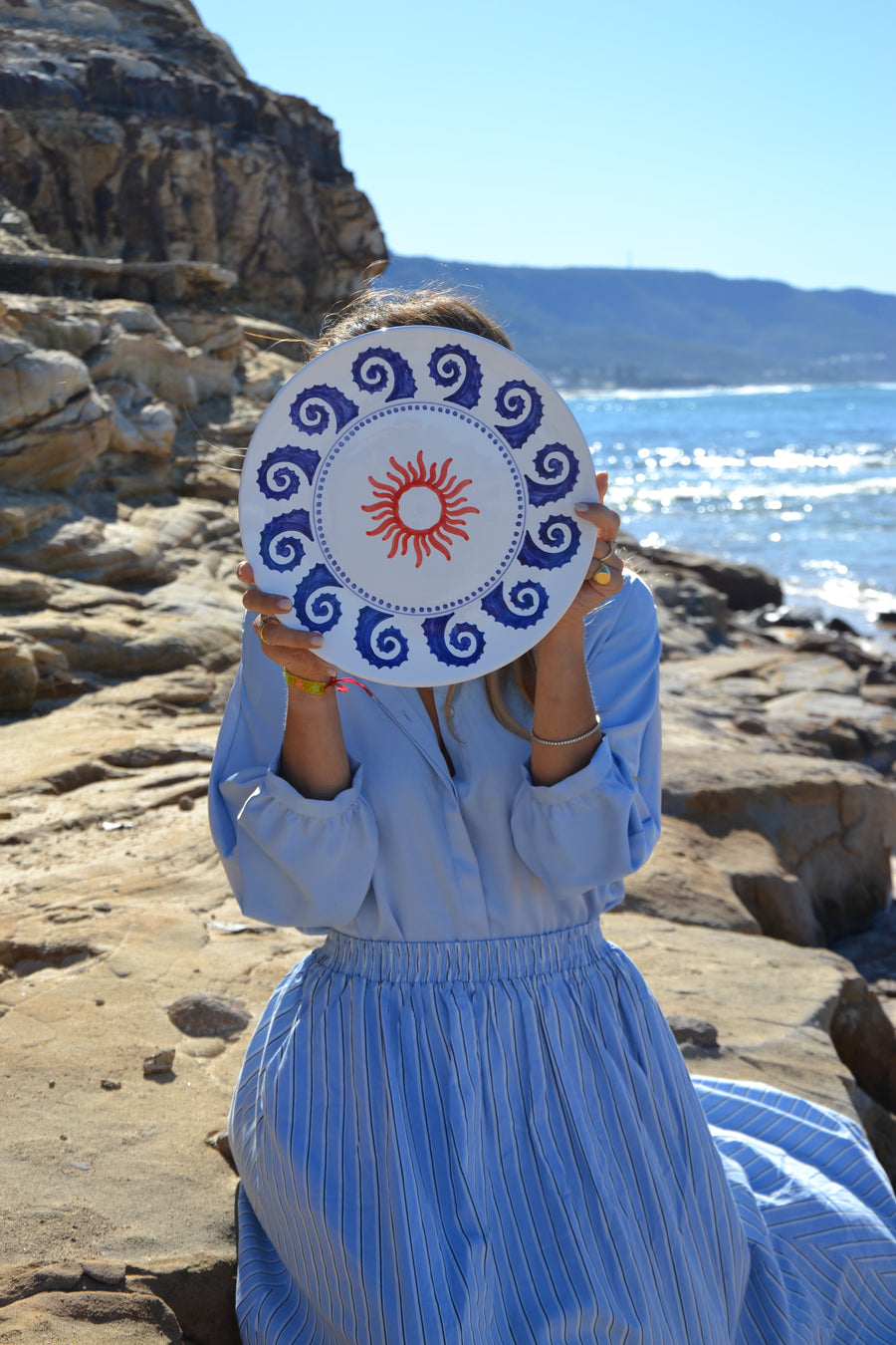 Person holding a circular object with a sun design against a rocky cliff background