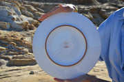 Person holding a white plate with a brown rim against a rocky background