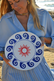 Woman holding a decorative plate with blue patterns and a red sun design.