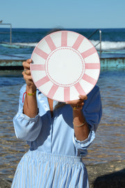Person holding a pink and white striped object by a body of water