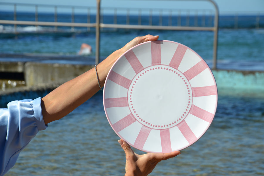 Person holding a pink and white decorative plate by the ocean