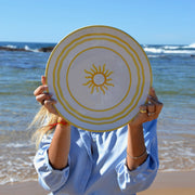 Person holding a sun-shaped disc with ocean and beach in the background
