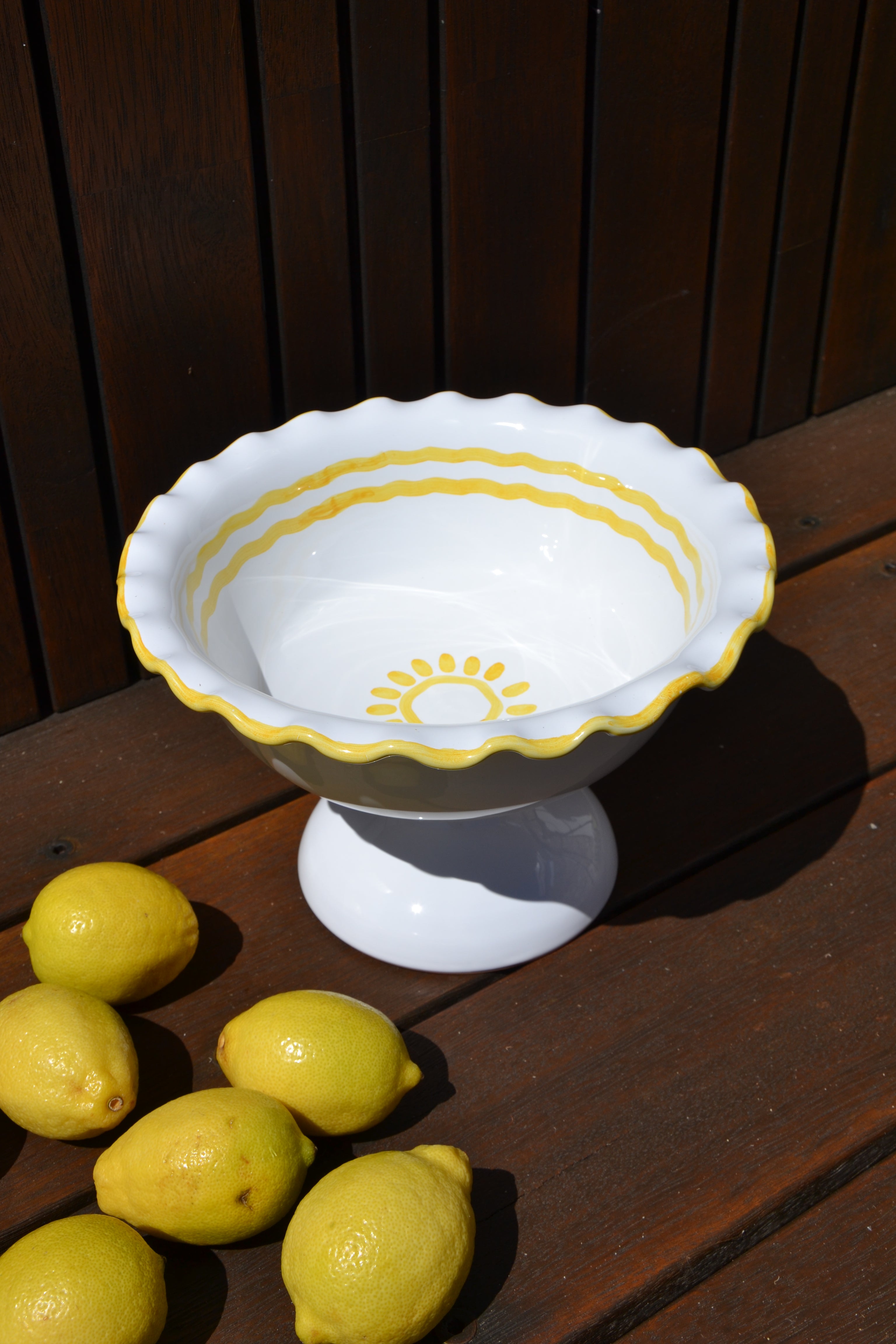 Decorative white bowl with yellow rim on a wooden surface with lemons.
