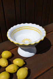 Decorative white bowl with yellow rim on a wooden surface with lemons.
