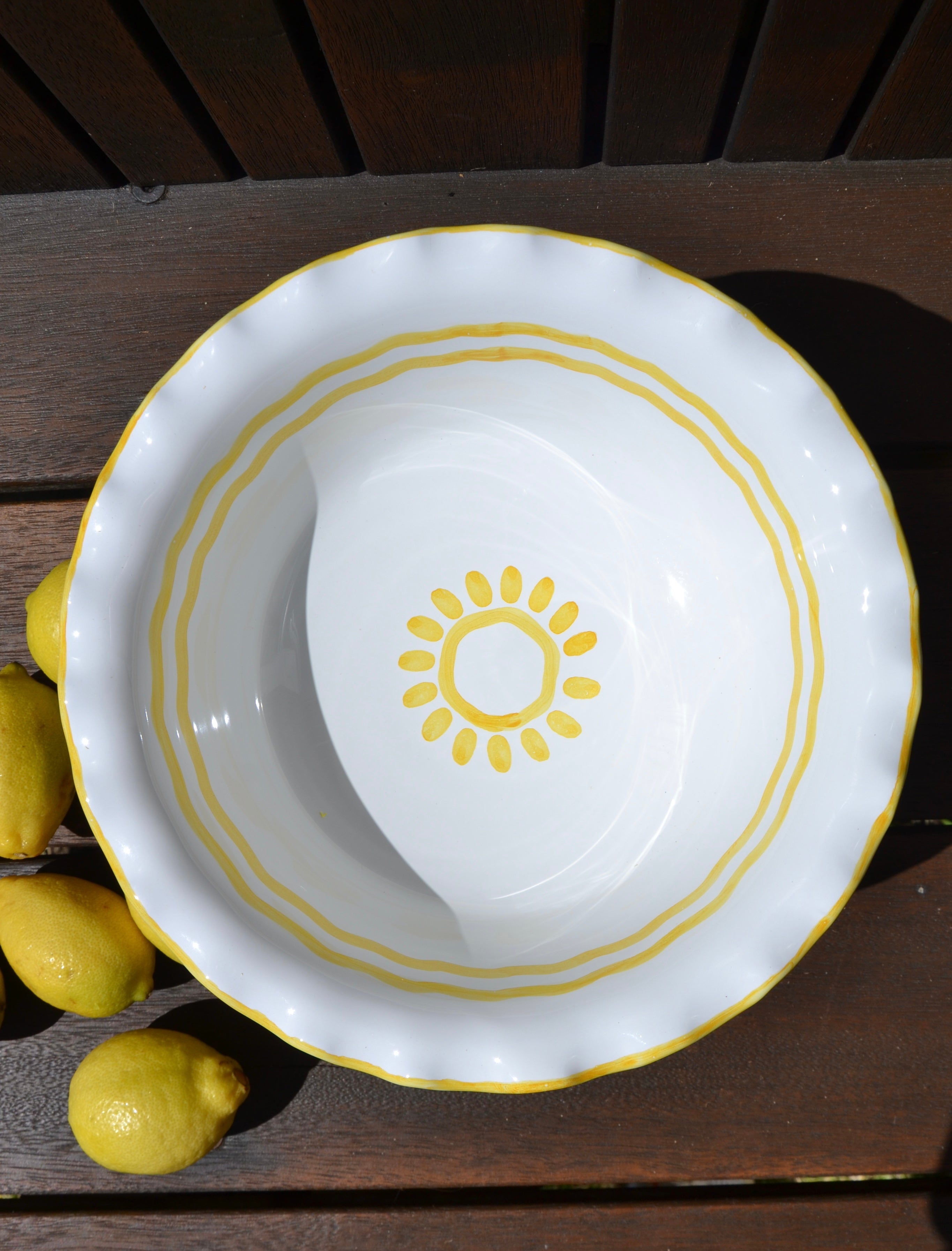 White bowl with yellow rim and sun design on a wooden surface with lemons.