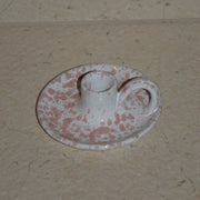 A small ceramic candleholder decorated with a pink speckled pattern, set on a beige stone surface.