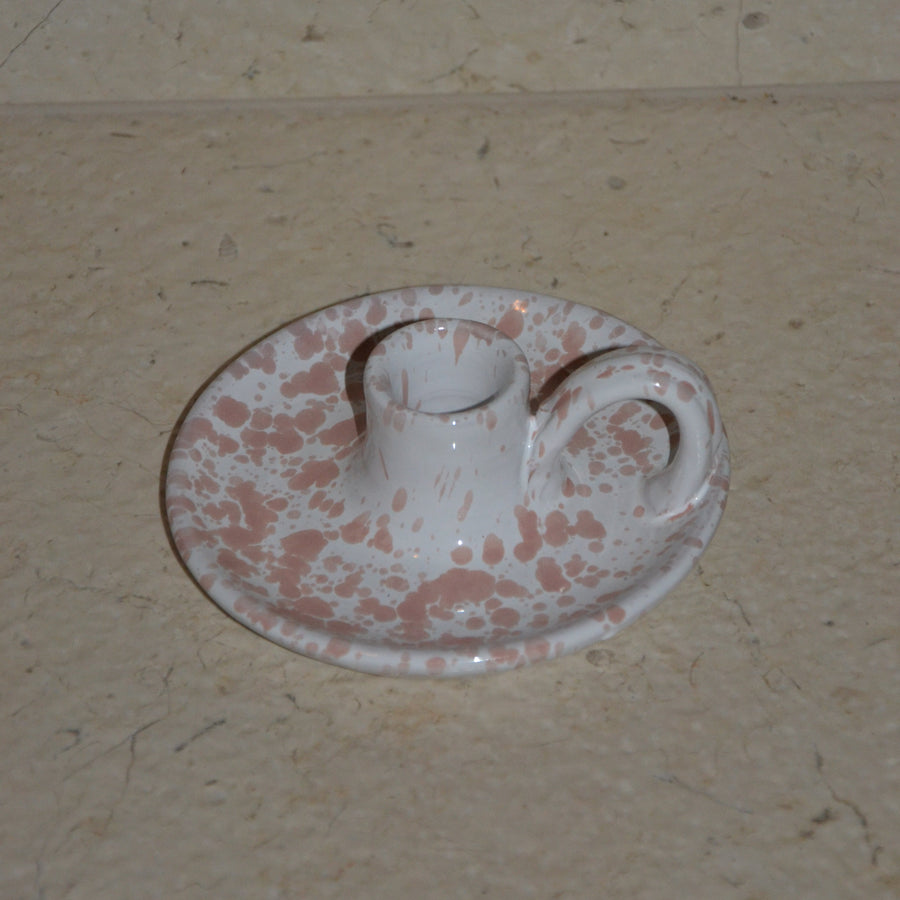 A small ceramic candleholder decorated with a pink speckled pattern, set on a beige stone surface.