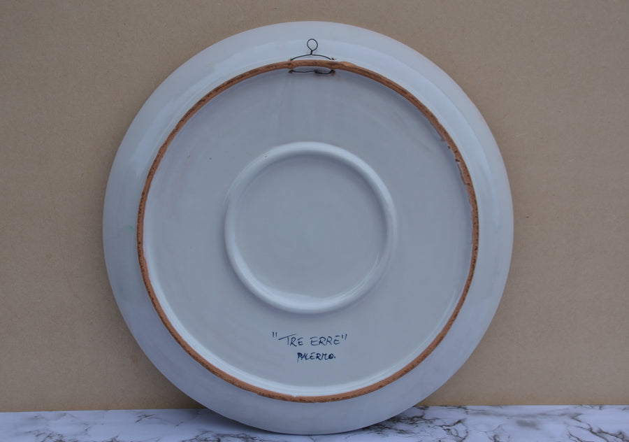 The back of a large white ceramic plate with a brown wooden hoop and metal hanging loop, featuring handwritten text 'THE ERRE' and 'PALERMO' on a beige background.